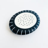 Large pebble shaped resin brooch cast in a black and white pattern of stripes and dots.  Displayed on white background.