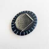 Back of large pebble shaped resin brooch cast in a black and white pattern of stripes and dots, showing the 2 pins mechanism. Displayed on white background.