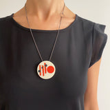 Large circular white resin pendant cast in a Midcentury Modern design of orange stripes and black polka dots. Hung on oxidised silver chain. Worn by model.