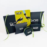 Display of TIKI branded packaging displaying various black boxes and pouches embossed with the Tiki logo in silver. Also showing is the green illustration Tiki postcard style business card.