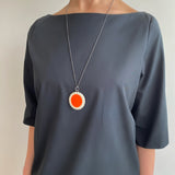 Large oval shaped red and white long pendant worn by model on a dark grey dress.
