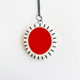 Large oval shaped pendant cast with a red centre and a white border which is inlaid with black stripes. It is hung on a silver chain.