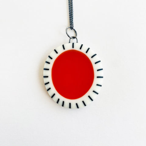 Large oval shaped pendant cast with a red centre and a white border which is inlaid with black stripes. It is hung on a silver chain.