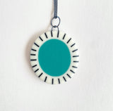 Large oval shaped pendant cast with a teal blue centre and a white border which is inlaid with black stripes. It is hung on a silver chain.