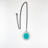 Large oval shaped pendant cast with a teal blue centre and a white border which is inlaid with black stripes. It is hung on a long oxidised silver chain.