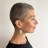 Leaf shaped resin earrings worn by model. They are cast in teal blue and white resin, and inlaid with black polka dots. Fitted with oxidised silver hooks.