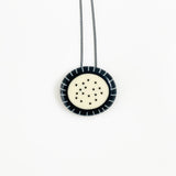 Necklace with a circular pendant featuring a white center and black dots on a white background