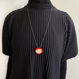 Person wearing a black ribbed sweater with a necklace featuring an orange and white pendant.