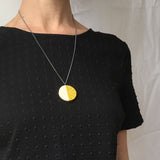 Minimalist circular pendant cast in lime and white resin. On long oxidised silver chain. Worn by model.