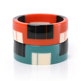 2 geometric resin bracelet cuffs, one in orange, the other in teal, both inlaid with black and white stripes