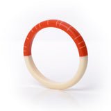 The modernist statement Lunula bracelet, handmade from paprika orange and creamy white resin. The minimalist design consists of two halves. One is plain white, the other is tangerine, inlaid with contrasting white lines.