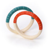 2 modernist Lunula resin bracelets. One cast in teal and white, the other in orange and white. Each coloured half is ornate with contrasting white lines.