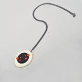 Oval shaped Nabu Necklace, handmade from black and white resin, and ornate with orange polka dots. Reversible, it can be worn  the other side, which is dotless. Smooth and tactile, the pendant hangs on a 60cm Sterling silver oxidised chain.