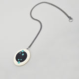 Pebble shaped Nabu pendant laying flat and displaying  its polka side, ornate with teal polka dots. It's showing the 60cm long Sterling silver oxidised chain. 