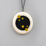 Pebble shaped reversible Nabu pendant, cast in white resin, in which is inserted a black resin centre. One side is plain, the other is decorated with delicate polka dots in mustard green resin. The pendant hangs on a 60cm Sterling silver oxidised chain.