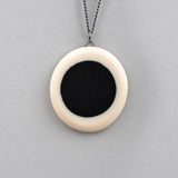 Pebble shaped reversible Nabu pendant, handmade from white resin in which is inserted a black centre. Image displaying the plain side. The other side is ornate with coloured polka dots. The pendant hangs on a 60cm Sterling silver oxidised chain.