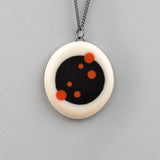 Oval shaped reversible Nabu necklace, handmade from white resin, inserted with a black centre. One side is plain, the other  is inlaid with 3 sizes of polka dots in orange resin. The pendant hangs on a 60cm Sterling silver oxidised chain.