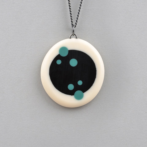Nabu Pendant. Oval shaped pendant made from white resin inserted with a black resin centre. The surface is ornate with various sizes of turquoise polka dots. Reversible, the other side is dotless. It hangs on a 60cm Sterling silver oxidised chain.