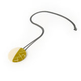 Mustard green and cream Lunula pendant, handmade from resin and Sterling silver. The minimalist design consists of one half in plain opaque cream resin, the other is cast in mustard green, inlaid with contrasting lines in white. It hangs on a 70cm long oxidised silver chain.