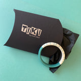 Modernist resin bracelet being prepared to be wrapped in Tiki branded pouch.