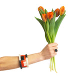 a selection of geometric statement cuff bracelets worn on model's arm, holding a bunch of flowers